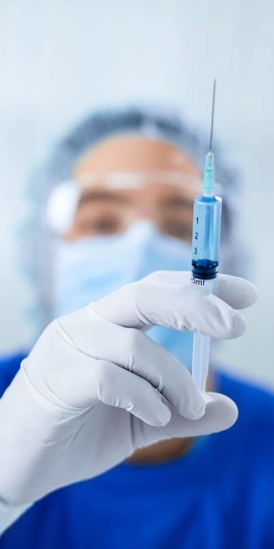 Врач нарколог в маске и медицинских перчатках держит шприц